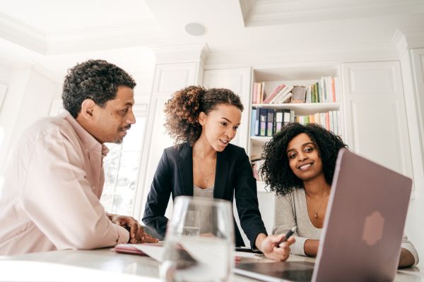 Three people sitting around a laptop computer working on a business planning tools.